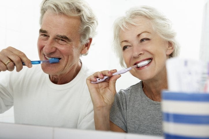 Image of two seniors brushing their teeth. Ivy Lane Dentistry offers periodontal maintenance services for senior patients in San Antonio, TX